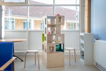 Photo of a wooden sculpture called 'Hospital Reimagined' by Jonathan Van Beek. Sculpture is surrounded by chairs in a bright room. 