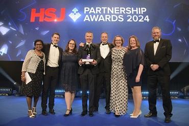 A group of people stand on stage holding an award under the words HSJ Partnership Awards 2024