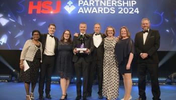 A group of people stand on stage holding an award under the words HSJ Partnership Awards 2024