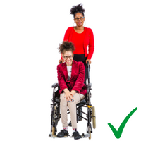 A person in a wheelchair with another person standing behind. Both are smiling at the camera.