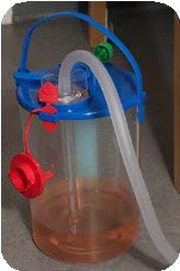 A clear bottle with a blue lid which the chest drain tubing is attached to. There is pink/orange liquid in the bottle.