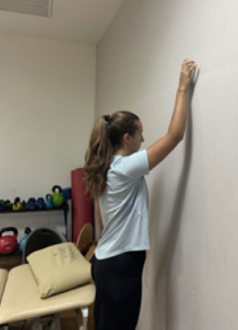 woman standing facing wall with arm raised and palm touching the wall