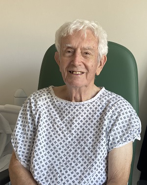 A person in a hospital gown sits in a chair, smiling