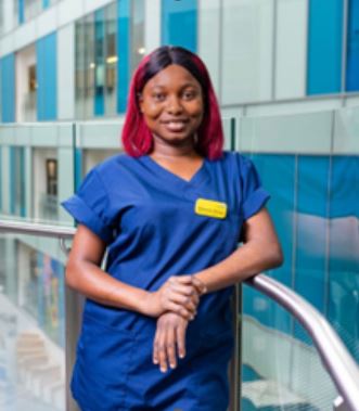 Omowumi Olamiju is a Ward Sister and Band 6 Internationally Educated Nurse at NBT, wearin g scrubs and standing by railing in the hospital's Brunel Building