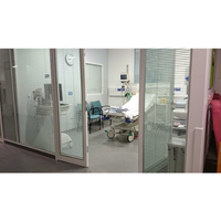 Patient room with a bed in the middle of the room, two chairs, and medical equipment