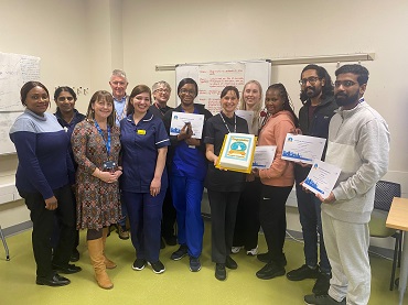 A group of people, some in nursing uniform stand together, holding certificates smiling at the camera