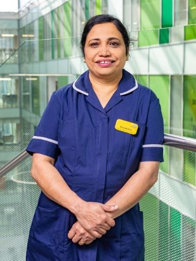 Sheela Shiji, Band 7 Team Leader and Clinical Co-Ordinator at NBT, wearing her uniform and standing in a glass stairwell