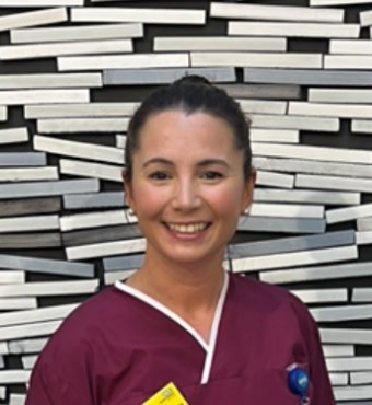 Woman standing against geometric background wearing maroon scrubs