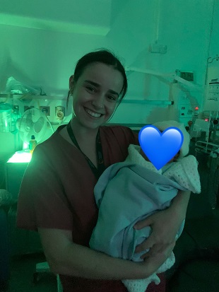 Midwife Rosie shares her experience of being a student at Southmead A woman in raspberry-coloured scrubs holds a baby, whose face is obscured by a blue heart