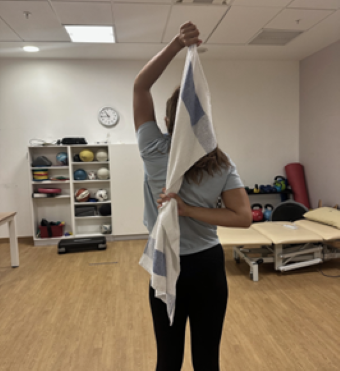 Woman holding a towel behind her back one arm at the level of ribs and one arm in the air