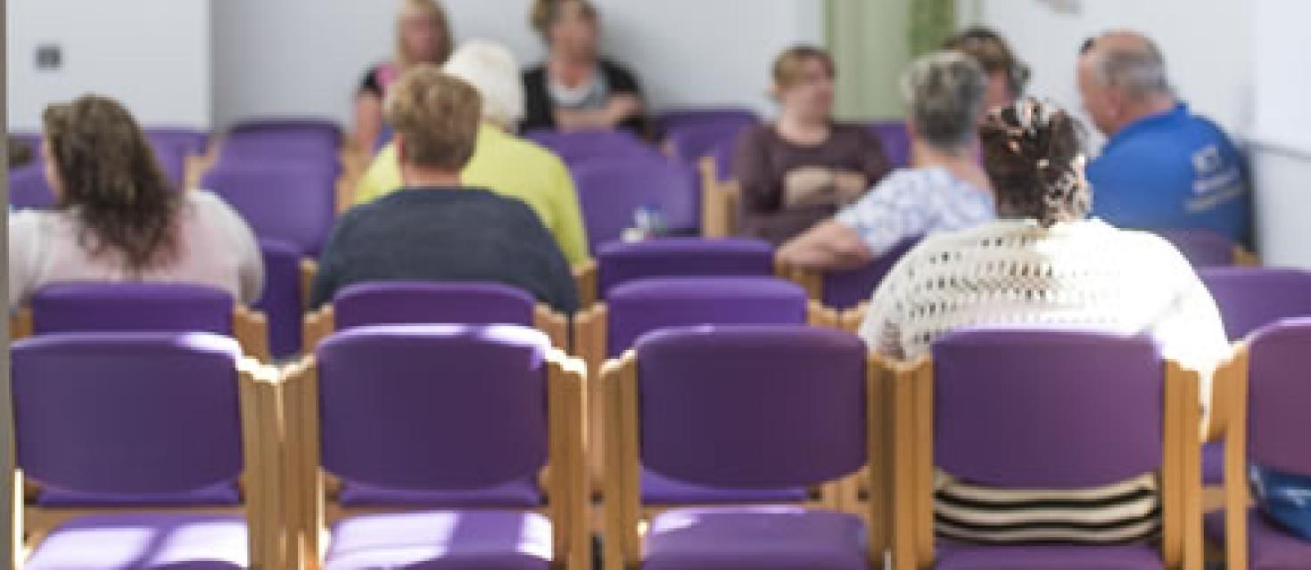 Clinic waiting room showing people from behind sitting on chairs waiting to be seen