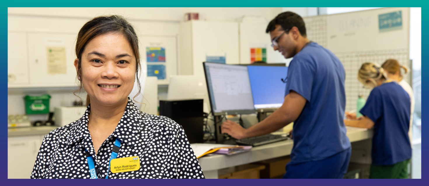 image of receptionist standing a ward hub with clinical staff in background