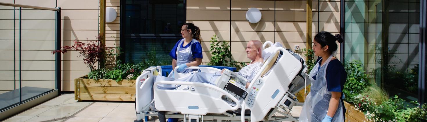 Photo of patient in a bed with two members of staff out on the ICU garden