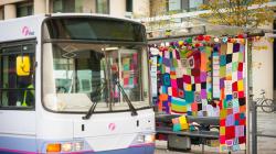 Bus pulls up at the Fresh Arts Knitted Bus Stop made by Ali Brown.