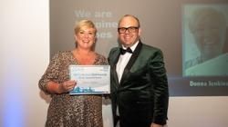 A woman in a sparkly dress receives a certificate from a man in a dinner suit