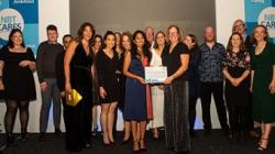 A large group of people stand on stage holding a certificate