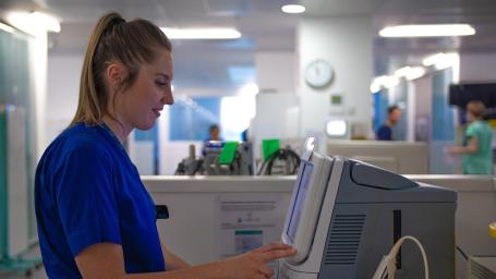 The image shows a healthcare worker using a Blood Gas analyser on a ward.
