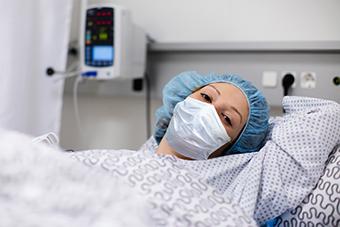 Patient wearing a face mask, lying in hospital bed