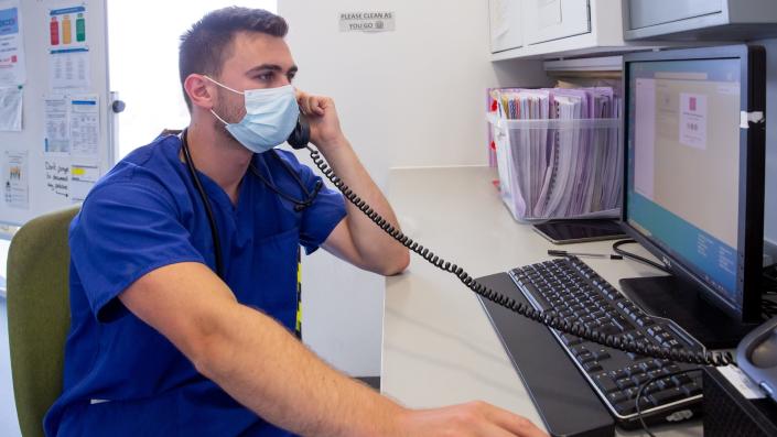 Clinical Fellow sitting at a PC and on the phone.