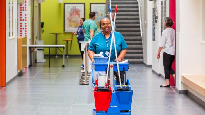 Happy cleaning lady with mops on a trolley