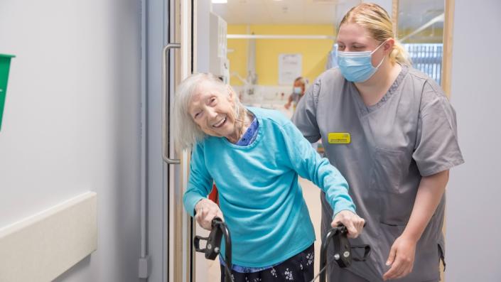 Healthcare support worker with a smiling patient using a walking aid