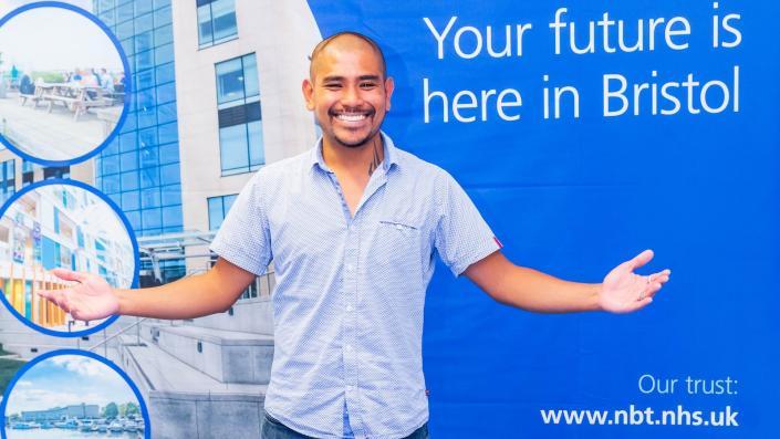 Recruitment Journey Event - Your Future is here in Bristol. Man smiling with arms spread wide in from of big blue NBT poster