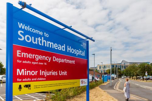 A blue, red and yellow sign saying "Welcome to Southmead Hospital" with information about the emergency department. The Brunel Building at Southmead Hospital can be seen in the background.