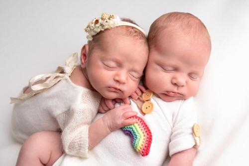 Twin babies lying together holding a rainbow in memory of their sister Florence