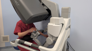 Consultant Gynaecology Surgeon Jessica Preshaw sits in front of a surgical robot, operating the robot's console with both hands.
