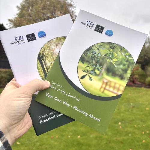 A hand holding up two booklets with trees and grass in the background