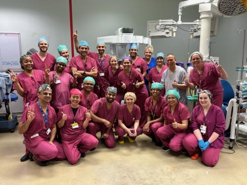 Surgical teams from the gynaecology high-intensity robotic-assisted surgery weekend. There are approximately 20 staff members all in clinical uniform grouped together in a theatre, smiling at the camera.
