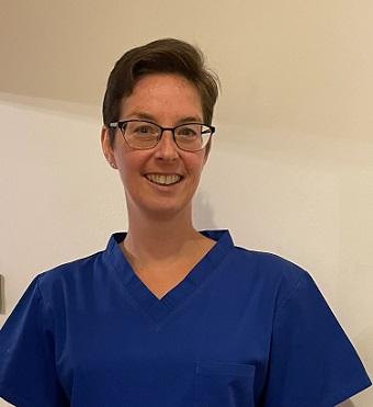 Jenni, smiling in her blue scrubs nurses' uniform