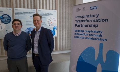 Two men, including James (right), stood together next to a banner that reads "Respiratory Transformation Partnership". 