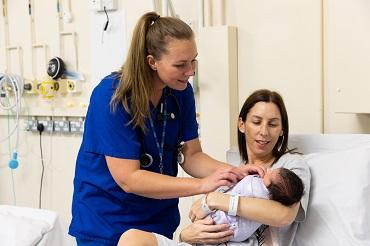 A person in blue scrubs checks a baby being held in someone's arms 