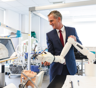 Secretary of State, Peter Kyle MP, wears a blue suit and is holding a white robotic surgical arm.