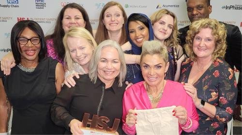 The award winners are grouped together smiling, holding their HSJ Award at the awards ceremony.