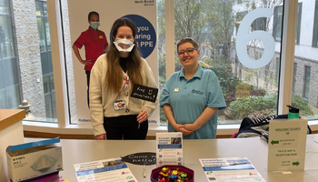 BSLC member Emma with NBT Staff member Ann who is wearing a clear face mask at a table with information on AIS in Gate 6 Brunel Building NBT.