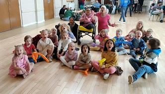 A group of children sitting on the floor and one in a wheelchair with a balloon
