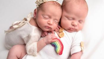 Twin babies lying together holding a rainbow in memory of their sister Florence