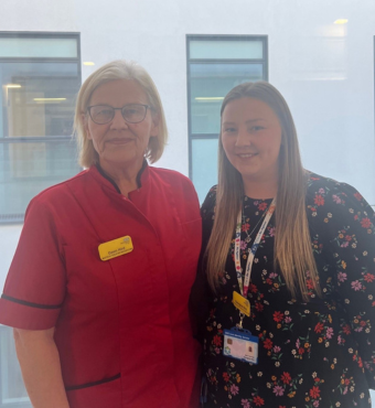 Dawn and her daughter Georgie, who both work at NBT, are stood together smiling. Dawn is wearing a red clinical uniform and Georgie is wearing a patterned dress.