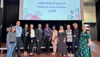 A group of people stand together in front of a sign that says "Thank you! Celebrating 20 years of Patient and Carer Partners at NBT"