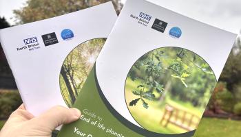 A hand holding up two booklets with trees and grass in the background