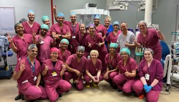 Surgical teams from the gynaecology high-intensity robotic-assisted surgery weekend. There are approximately 20 staff members all in clinical uniform grouped together in a theatre, smiling at the camera.