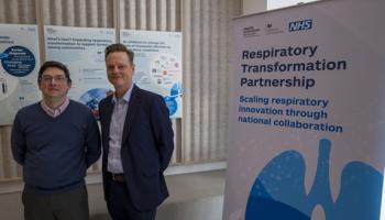 Two men, including James (right), stood together next to a banner that reads "Respiratory Transformation Partnership". 