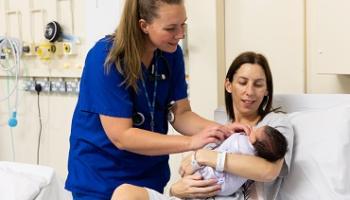 A person in blue scrubs checks a baby being held in someone's arms 