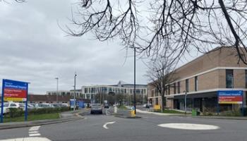 A mini roundabout with two hospital signs, a road and buildings