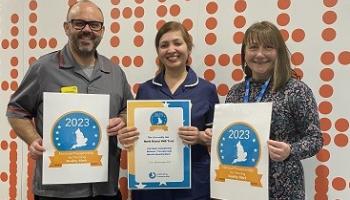 A man in dark grey nurse tunic, a woman in navy nurse tunic and a third woman stand holding certificates, smiling