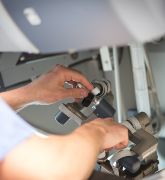 Two hands operate a silver robotic surgery console