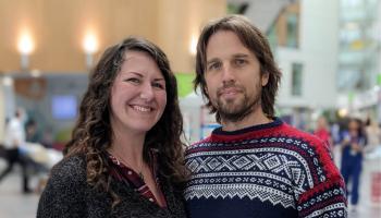 Kate and Neil are stood in the atrium of the Brunel building at Southmead Hospital smiling at the camera