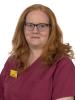 A woman in raspberry coloured scrubs looking at the camera